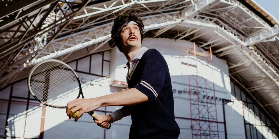 A man playung tennis in In Olympic Indoor tennis court.